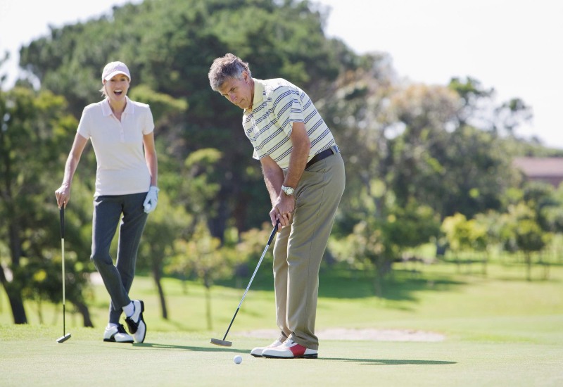 A man and woman play golf on a green field without elbow pain in Maryland
