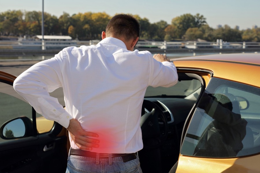 A man stands next to his car, holding his back after an auto accident in Maryland