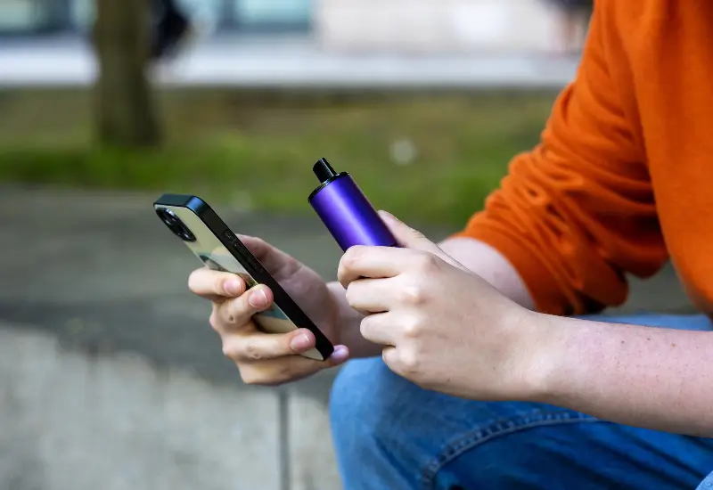 A man sits outside vaping and looking at his phone in Maryland