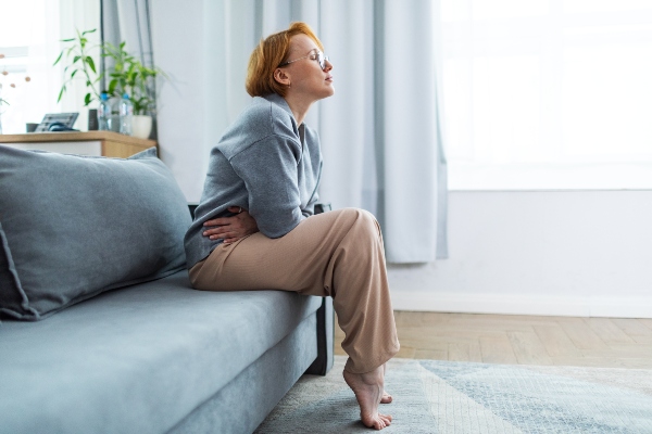 Woman holding abdomen in pain while sitting on couch